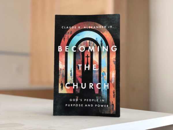 A photograph of the book Becoming the Church by Claude R Alexander Jr propped up on a table